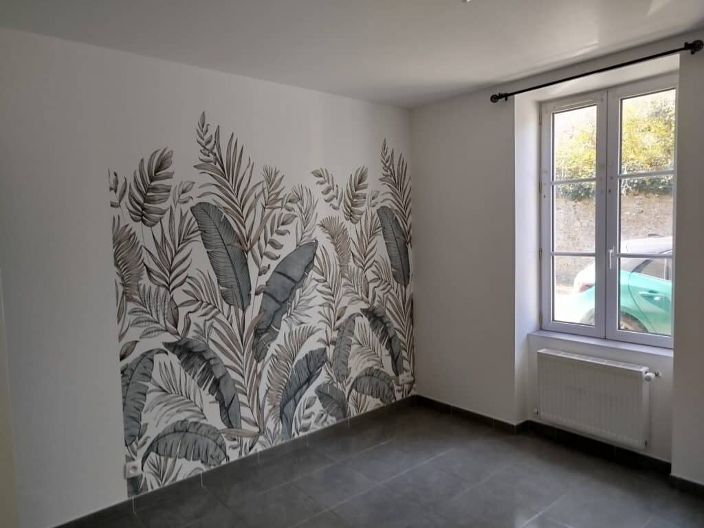 Pièce vide lumineuse avec mur décoré d'un papier peint à motifs feuilles tropicales gris et blanc. Fenêtre, radiateur, carrelage gris au sol.