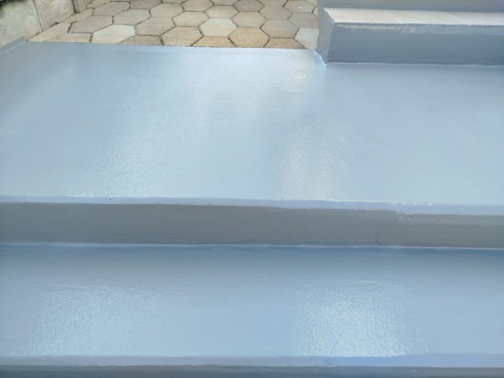 Marches et patio extérieurs fraîchement peints en bleu-gris, avec texture granuleuse. Dalles hexagonales en arrière-plan.